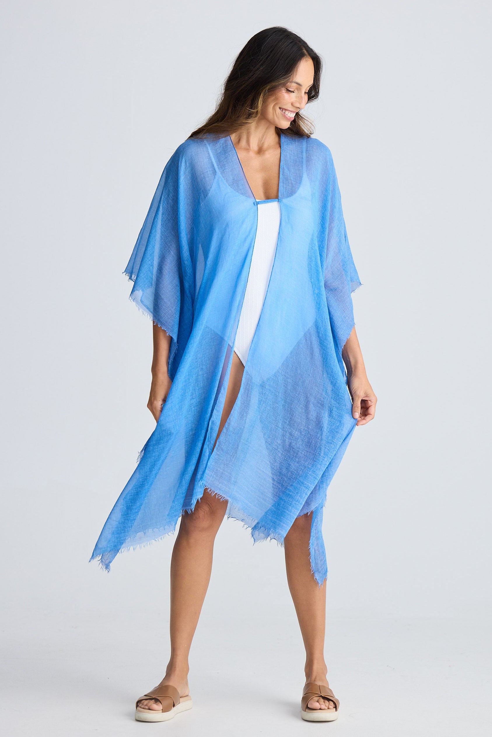 Woman wearing a light blue kimono-style garment over a white dress on a plain background