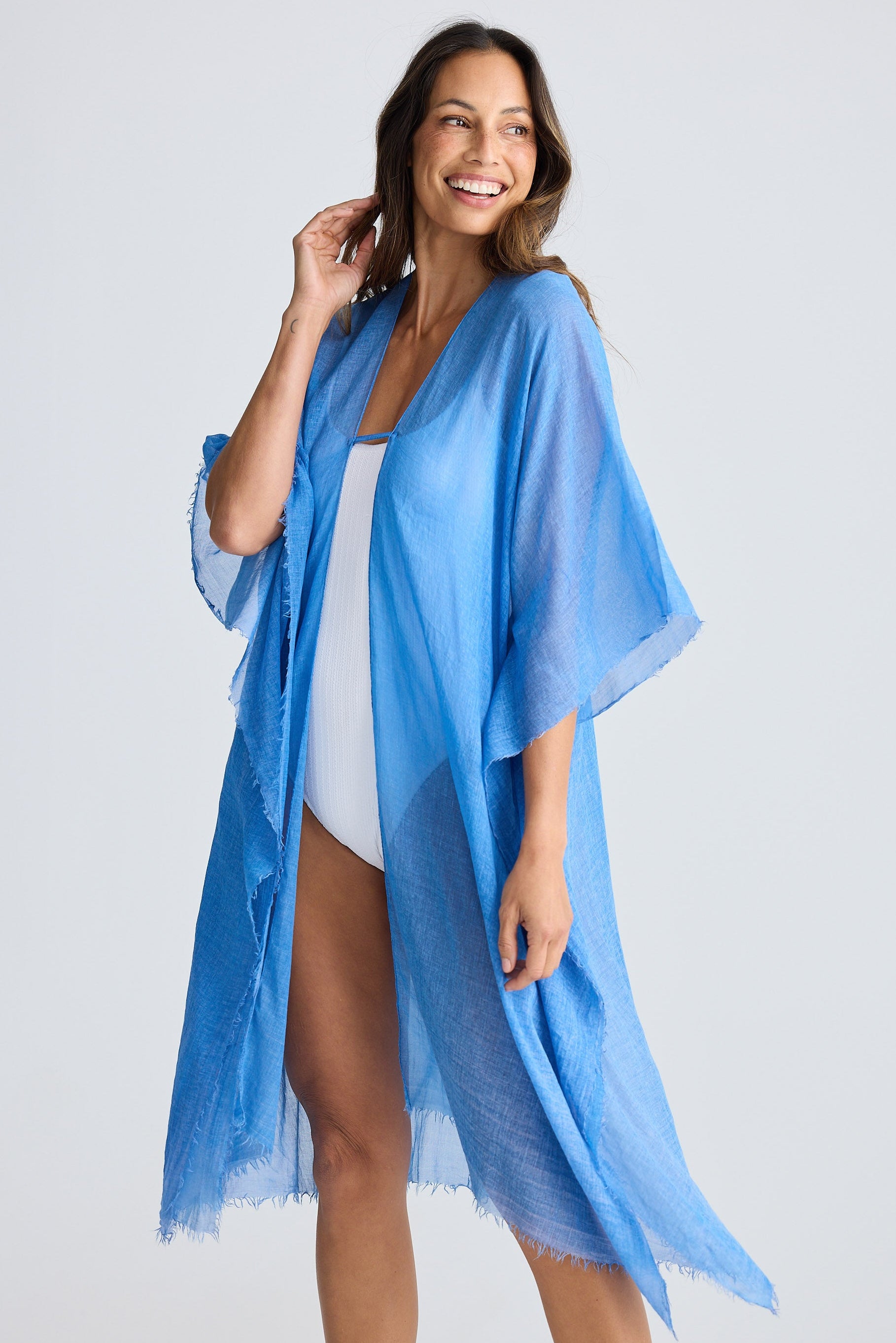 Woman wearing a blue kimono-style cover-up over a white top on a light gray background