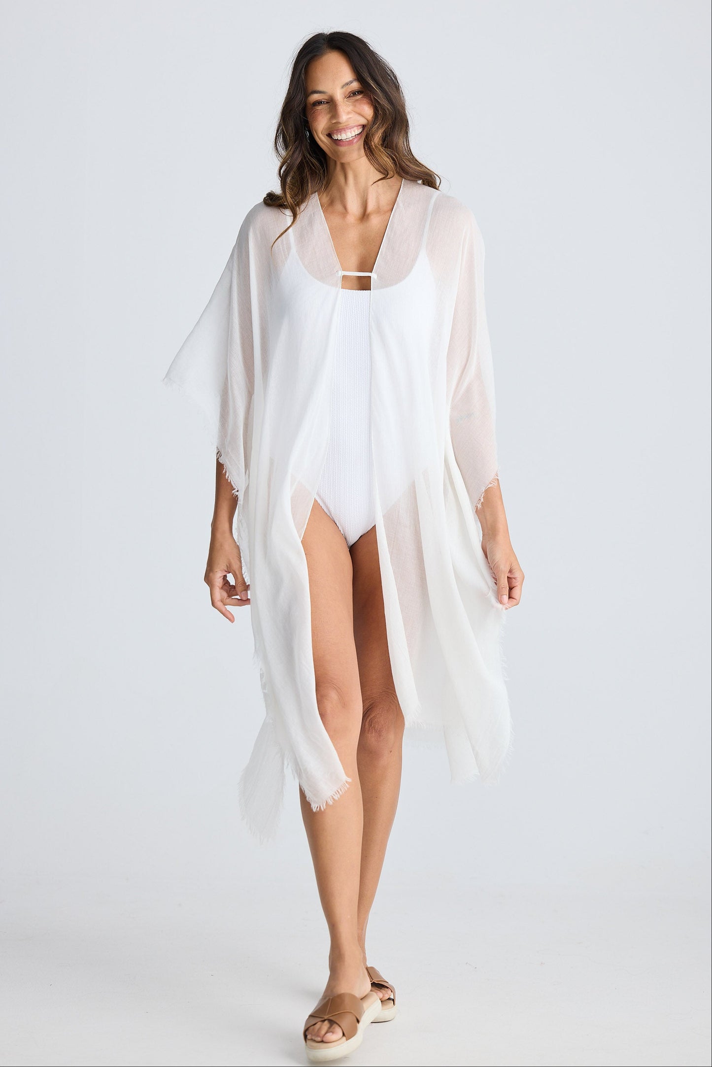 Woman wearing a white cover-up over a swimsuit on a plain background