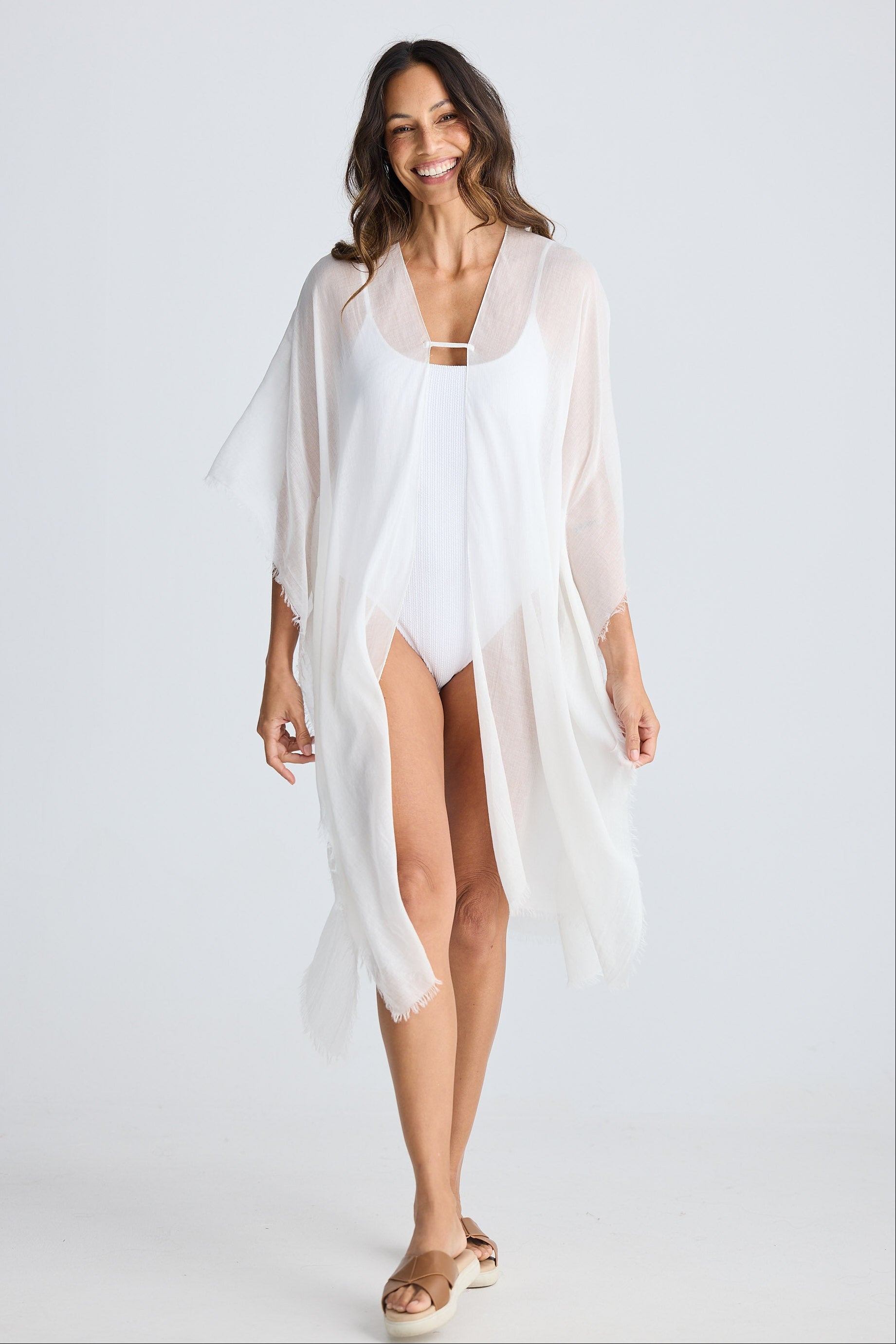 Woman wearing a white cover-up over a swimsuit on a plain background