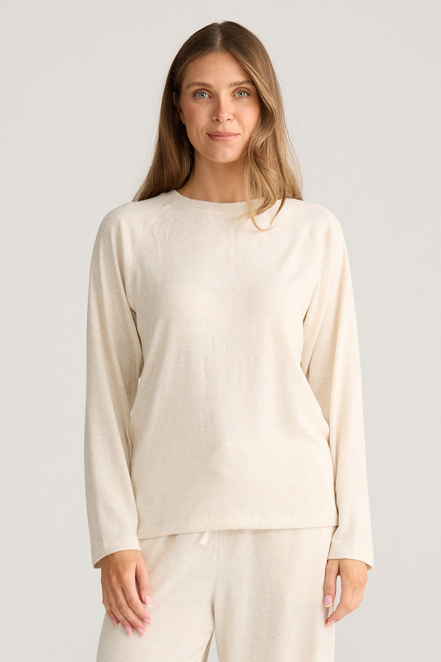 Woman wearing a beige long-sleeve top and pants on a light gray background