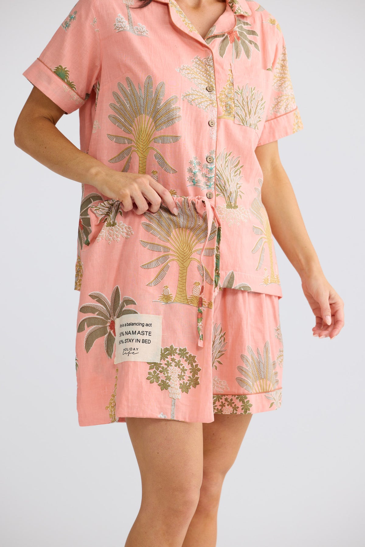 Close-up of Namaste Pyjama Set in baby pink palm, showing the shirt, shorts and matching drawstring bag.