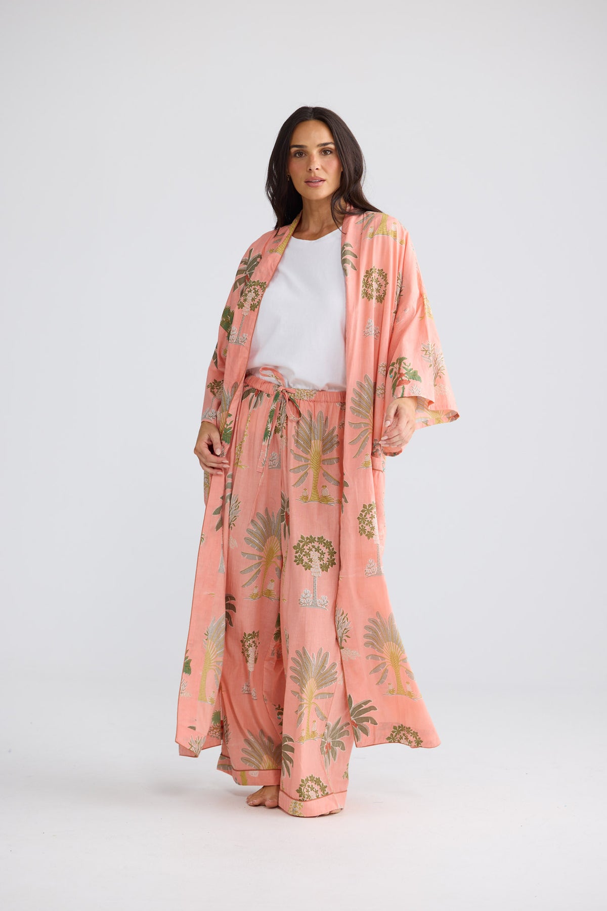 Model wearing Namaste Robe in baby pink palm, open over a white tee and matching pant, front view.
