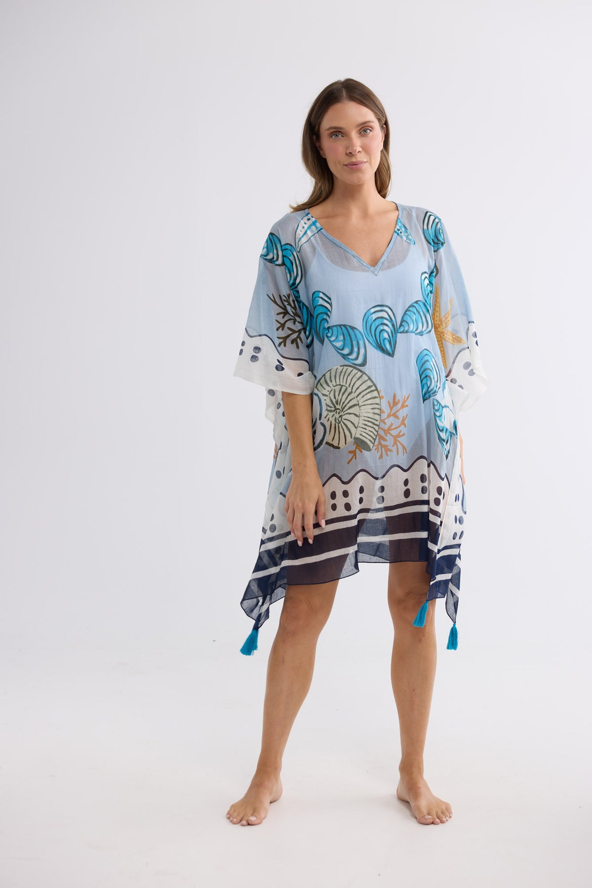 Model wearing Stella Kaftan in starfish dreams, front view. V-neckline, shell print, tasselled corners.