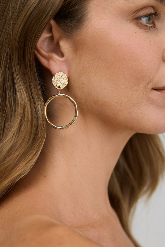 Close-up of a woman wearing gold hoop earrings with a neutral background