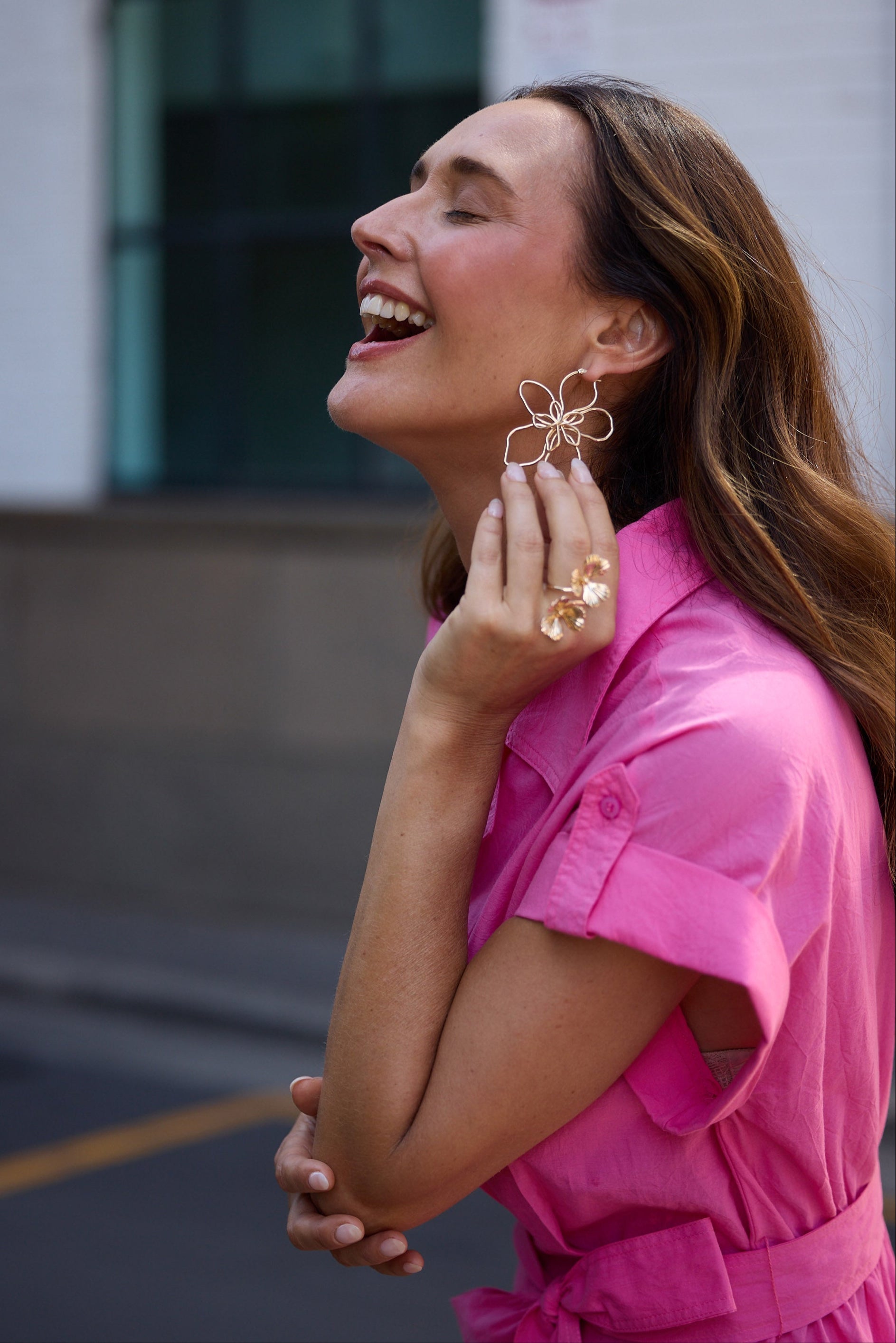Woman in a pink dress wearing gold earrings and rings outdoors.