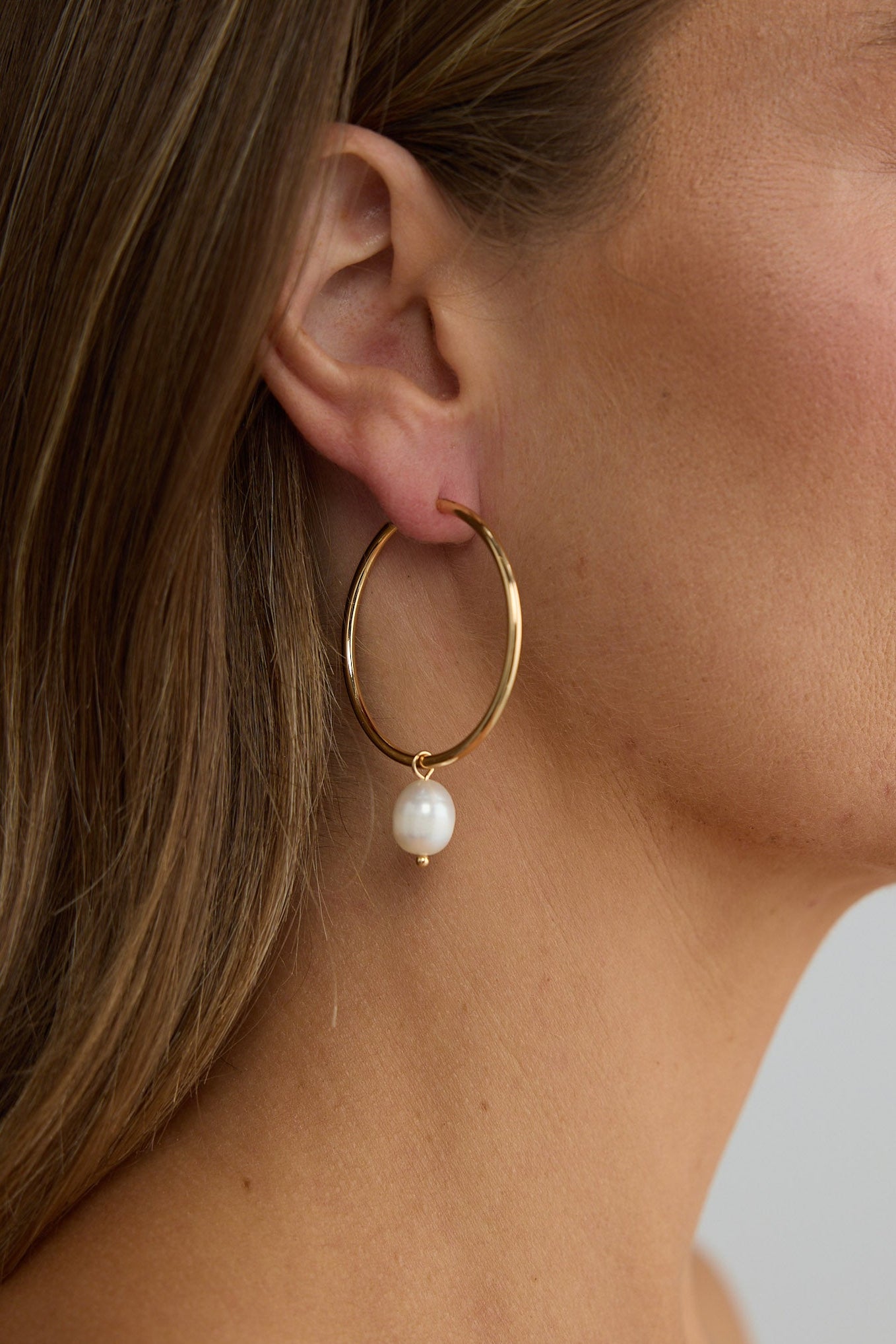 Close-up of a woman wearing gold hoop earrings with a pearl accent.