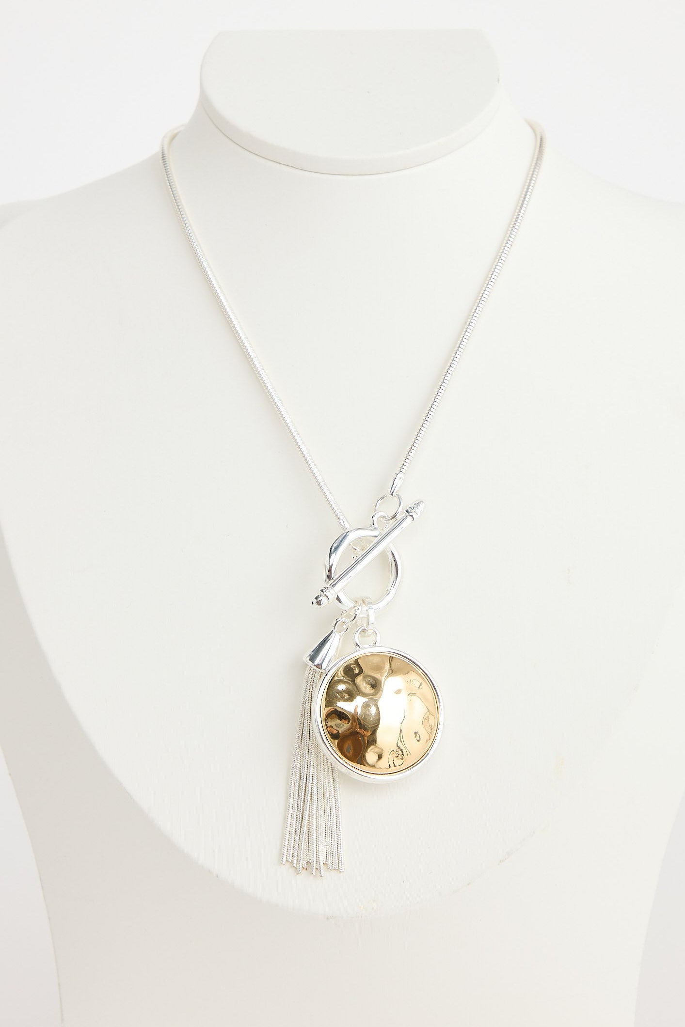 Necklace with a large round pendant and tassel on a mannequin against a white background