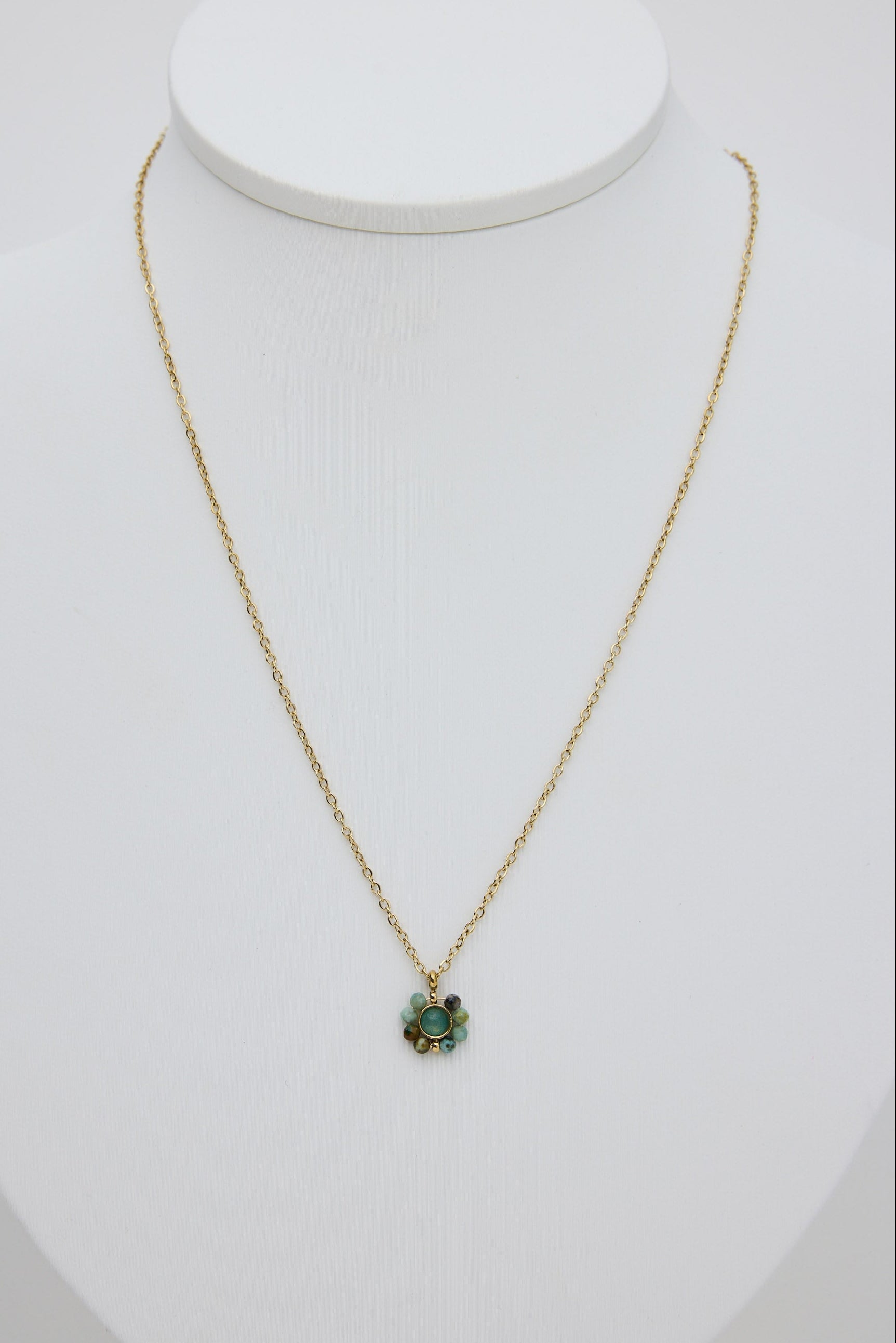 Gold necklace with a green pendant on a white mannequin bust