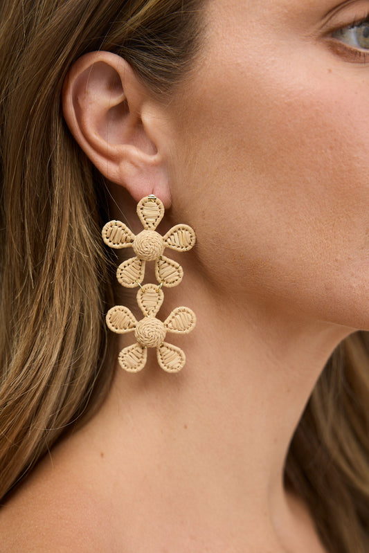Close-up of a woman wearing natural floral earrings against a neutral background