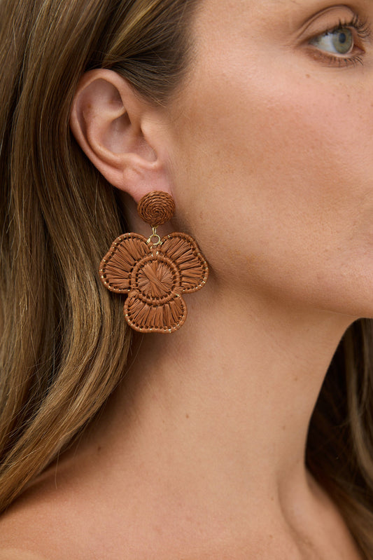 Close-up of a woman wearing brown floral earrings with a neutral background