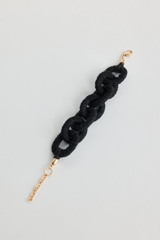 Black braided hair tie with gold clasp on a light gray background