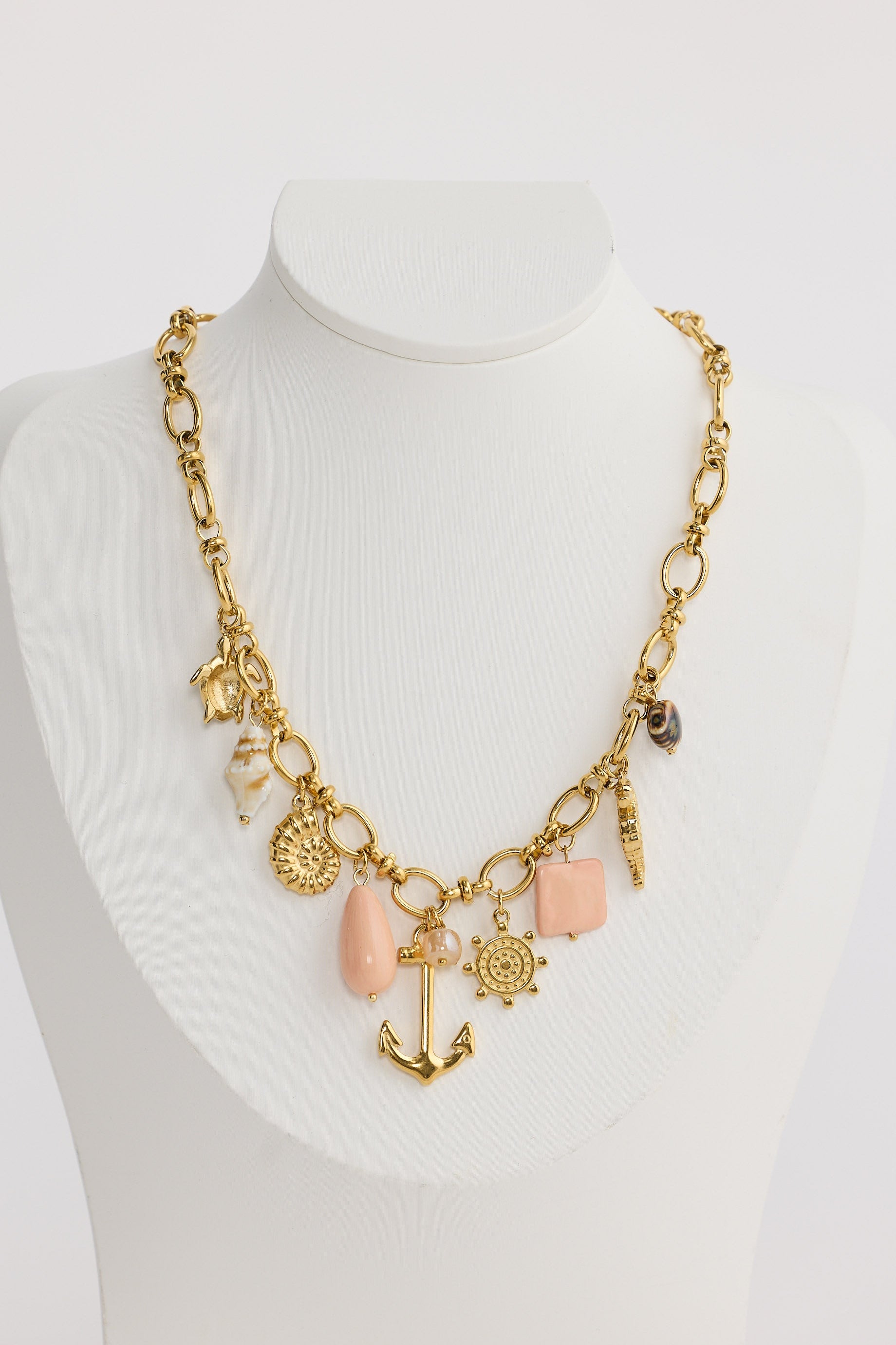 Gold necklace with various charms on a mannequin against a white background