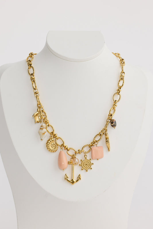 Gold necklace with various charms on a mannequin against a white background