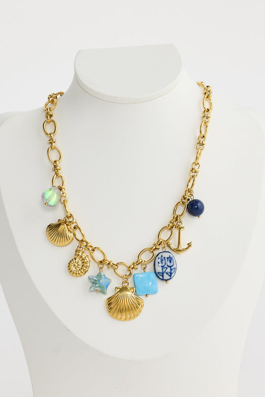 Gold necklace with various charms on a mannequin bust against a white background