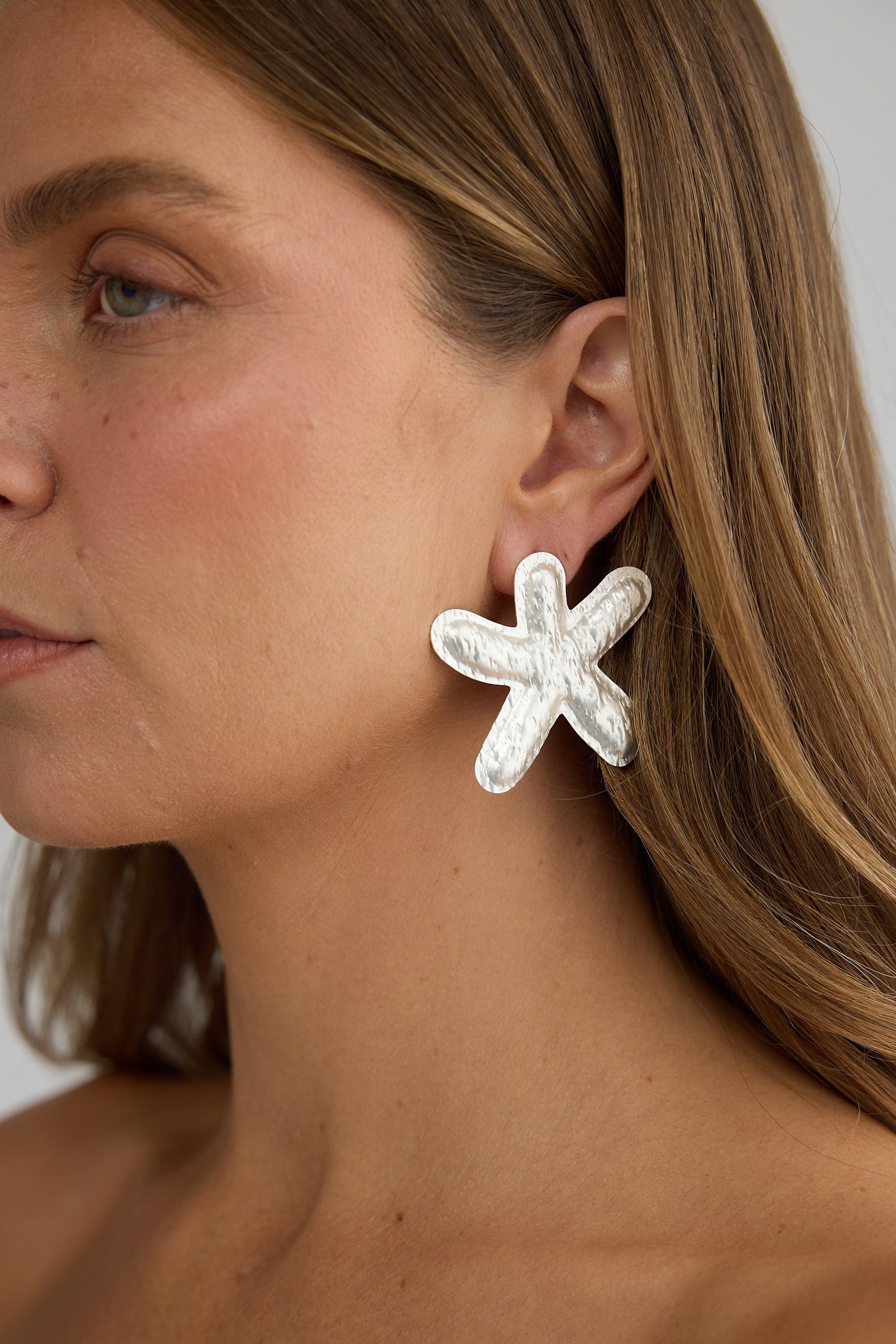 Close-up of a woman wearing starfish-shaped earrings against a neutral background