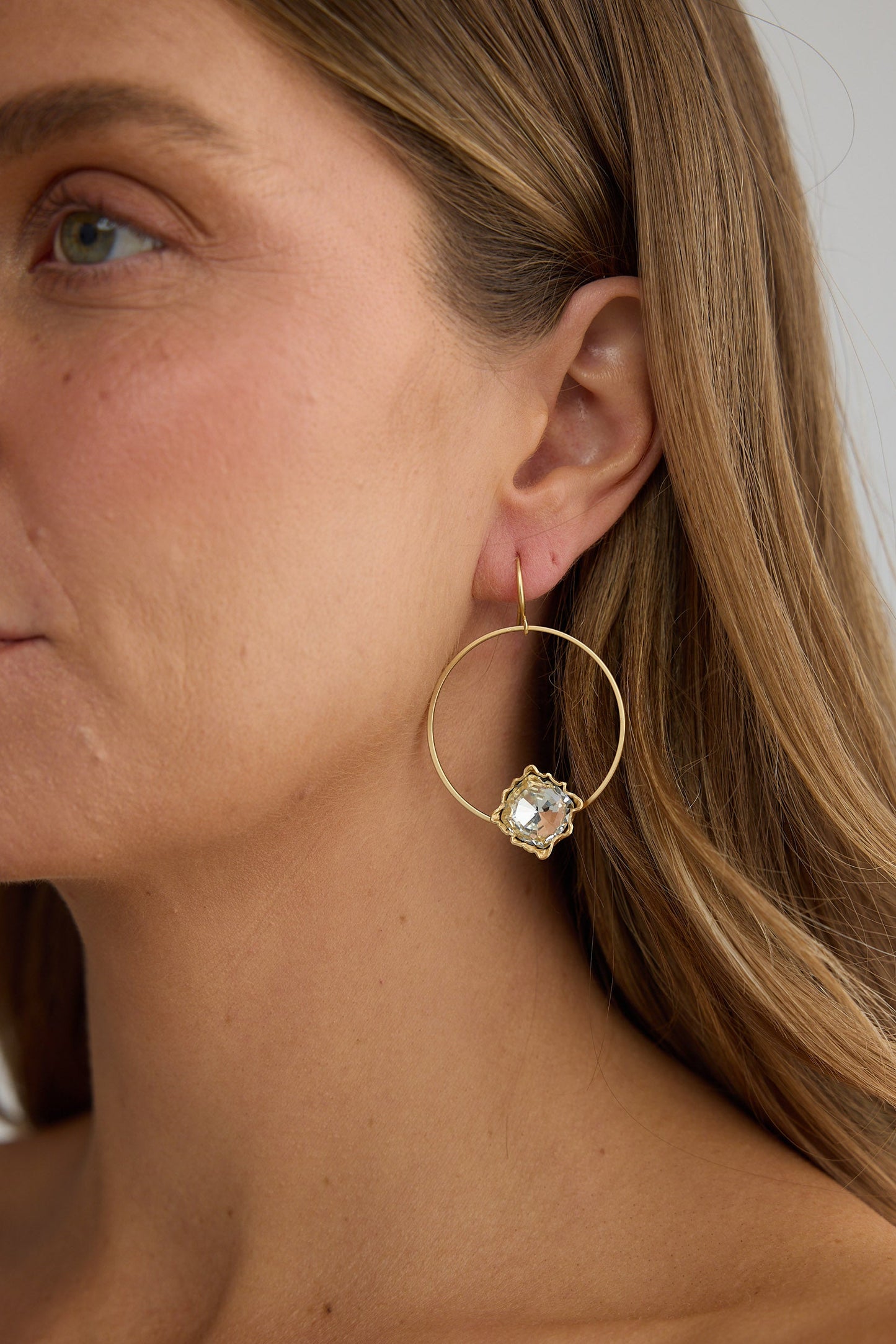 Close-up of a woman wearing gold hoop earrings with a clear gemstone.