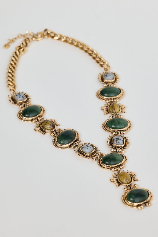 Gold necklace with green gemstones on a light gray background