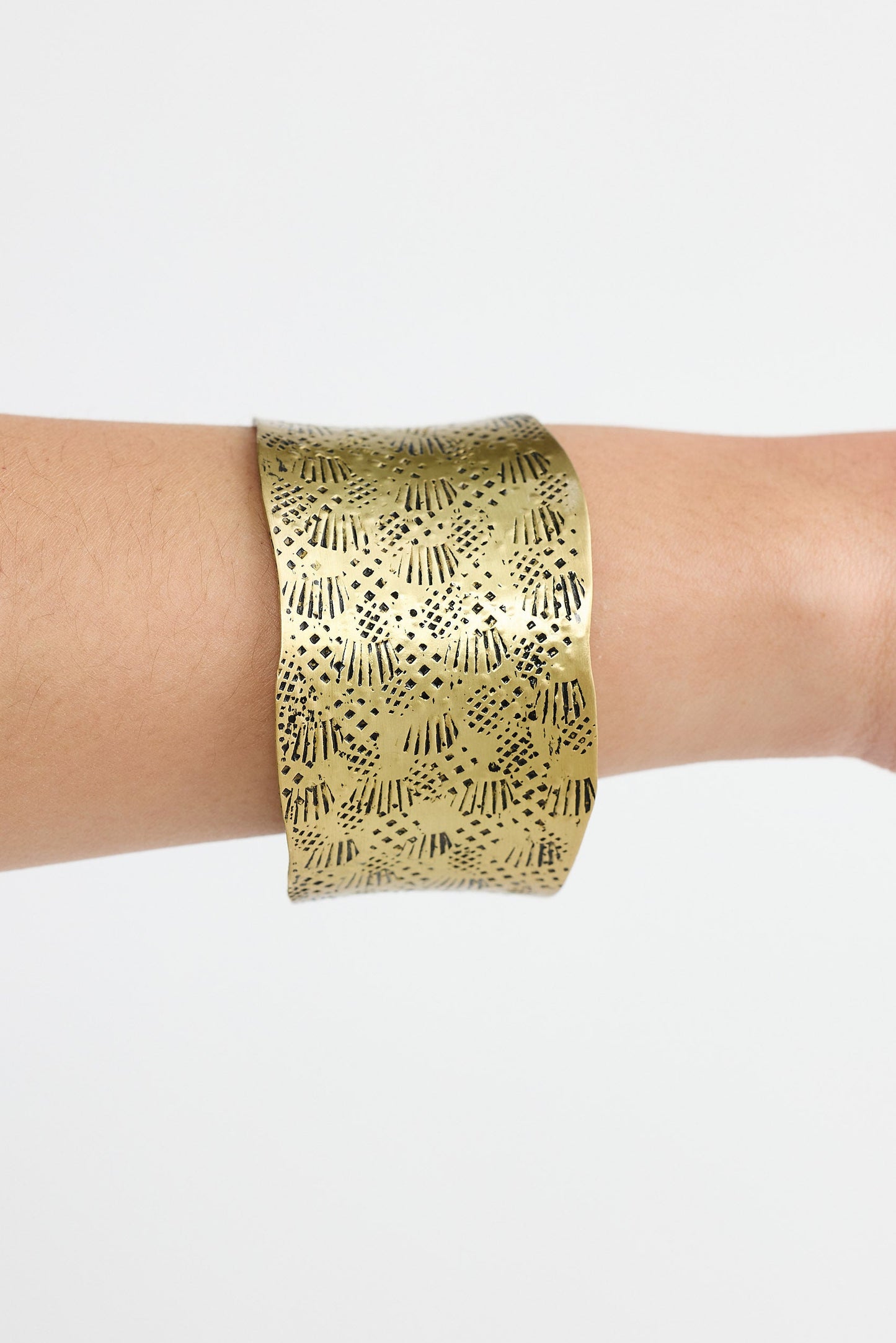 Gold bracelet with geometric pattern on a wrist against a white background