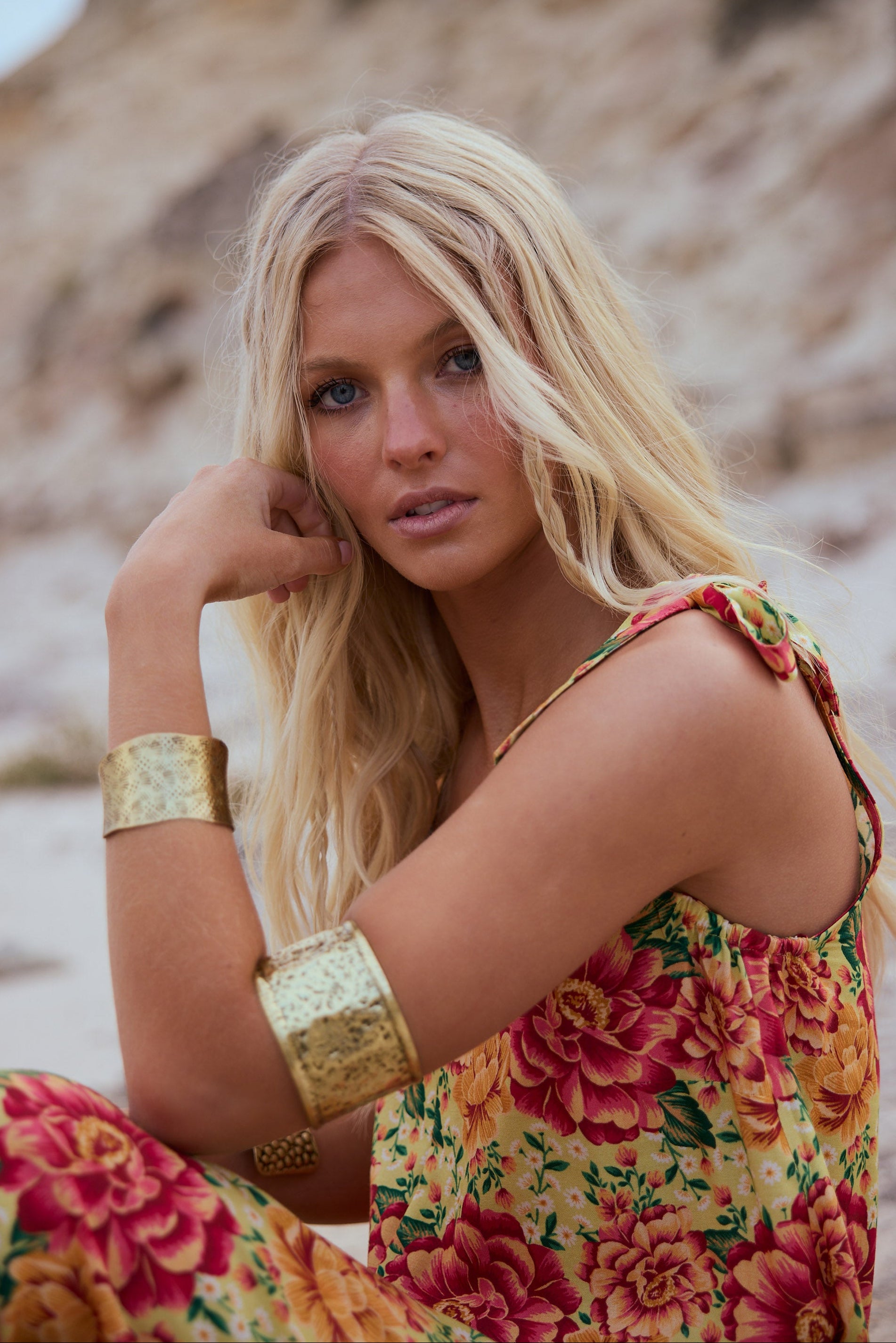 Woman in a floral dress with gold arm bands against a natural background