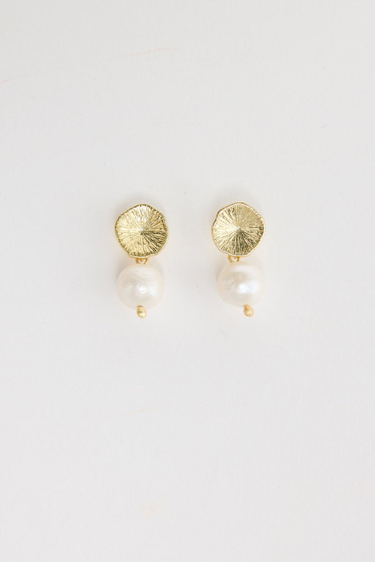 Pair of gold-tone drop earrings with a textured hammered disc stud and a single freshwater pearl drop with a small gold bead below, laid flat on a white background