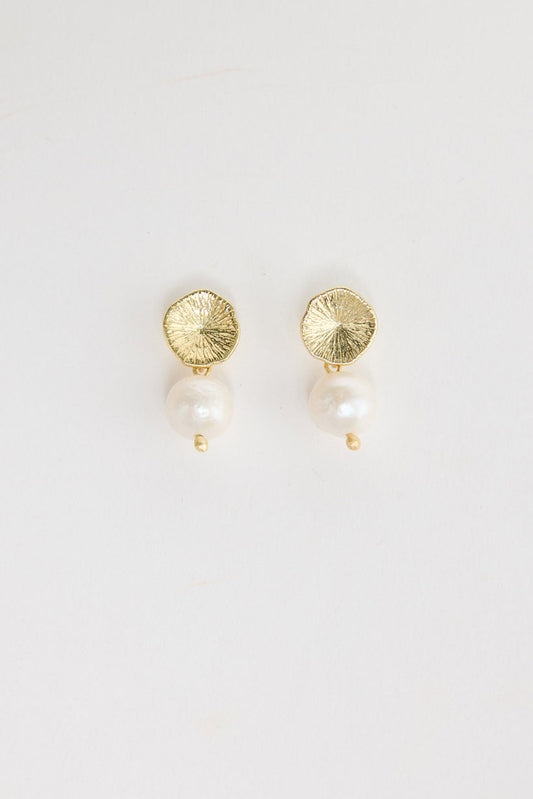 Pair of gold-tone drop earrings with a textured hammered disc stud and a single freshwater pearl drop with a small gold bead below, laid flat on a white background