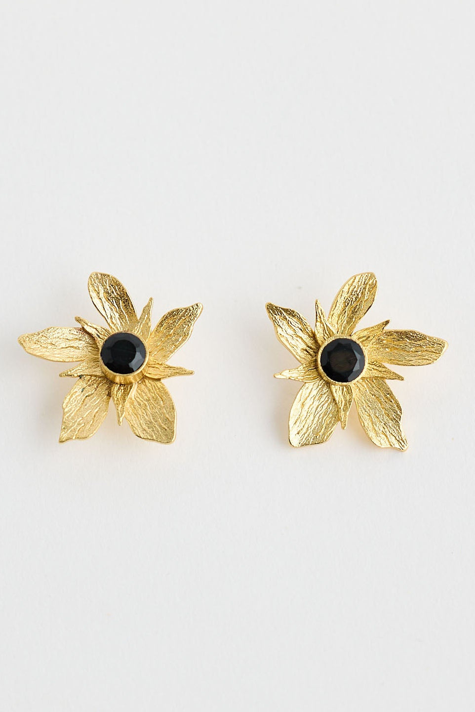 Gold flower-shaped earrings with black centers on a white background