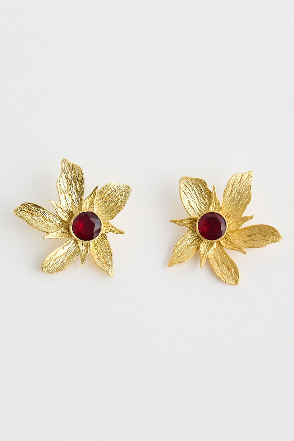 Gold flower-shaped earrings with red centers on a white background