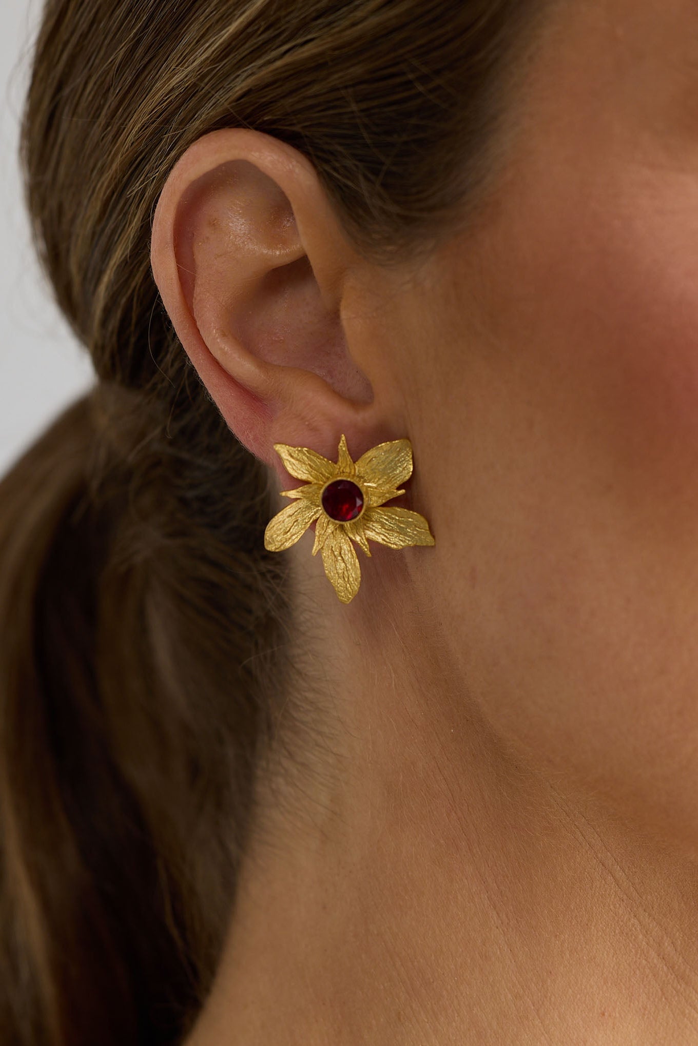 Close-up of a woman wearing gold flower earrings with a blurred background