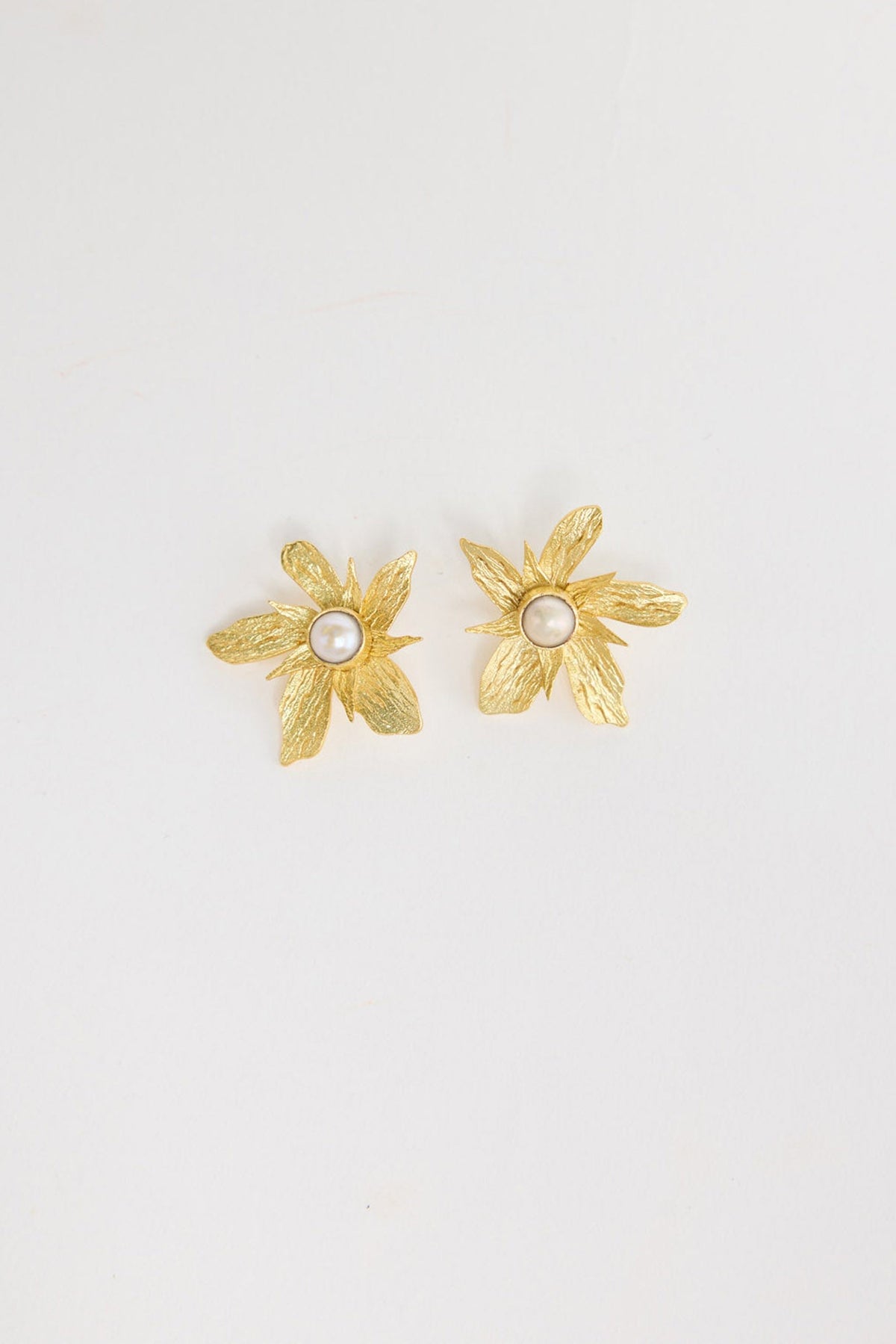Pair of large gold-tone flower stud earrings with textured brushed petals and a pearl centre, laid flat on a white background
