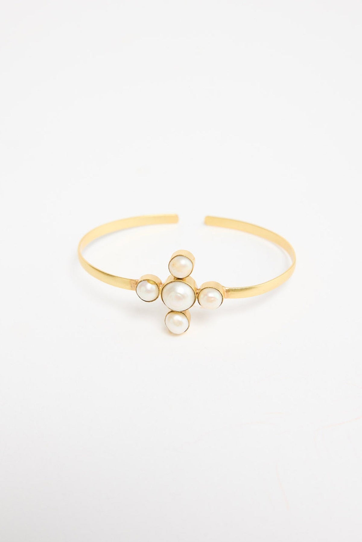 Open gold-tone cuff bracelet with a cross-shaped cluster of five freshwater pearls at the centre, shown at an angle on a white background