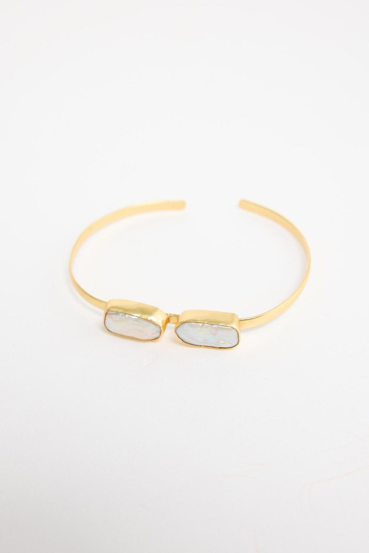 Open gold-tone cuff bracelet with two rectangular freshwater pearl stones set side by side in bezel settings at the centre, shown at an angle on a white background