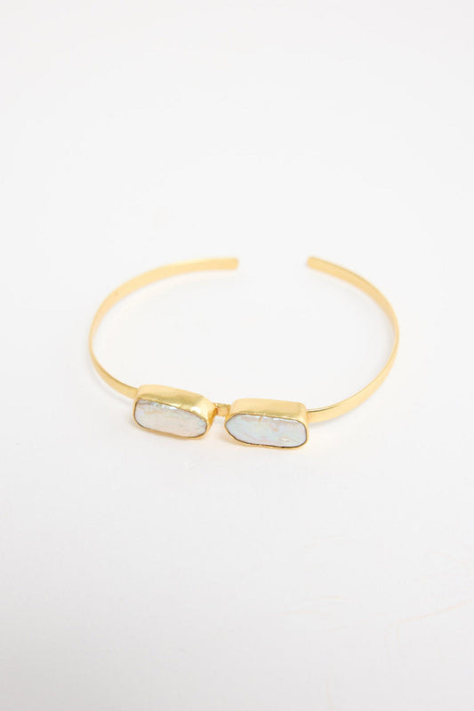 Open gold-tone cuff bracelet with two rectangular freshwater pearl stones set side by side in bezel settings at the centre, shown at an angle on a white background
