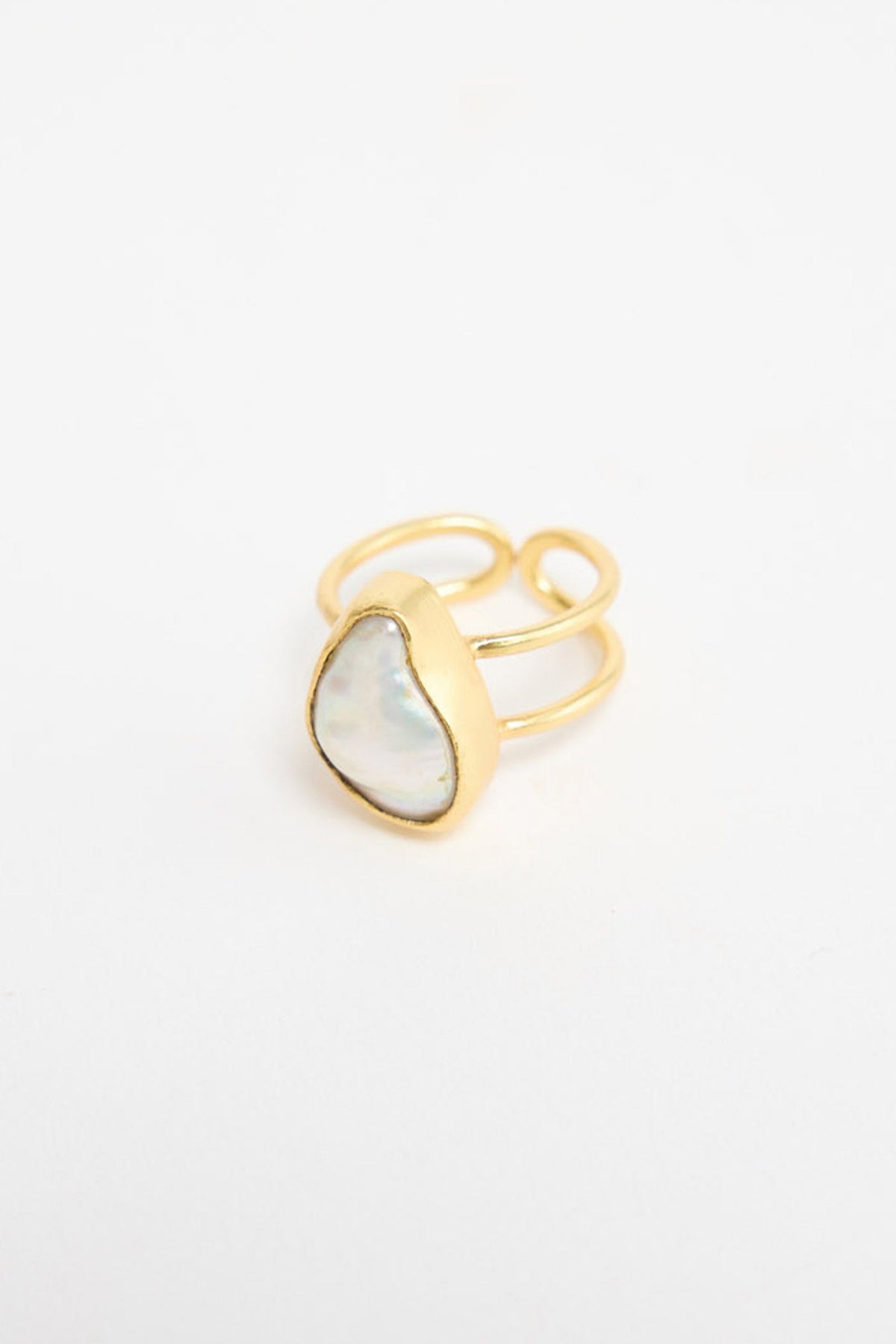 Large oval gold-tone statement ring with a cream mother-of-pearl resin stone in a hammered bezel setting, shown at an angle on a white background