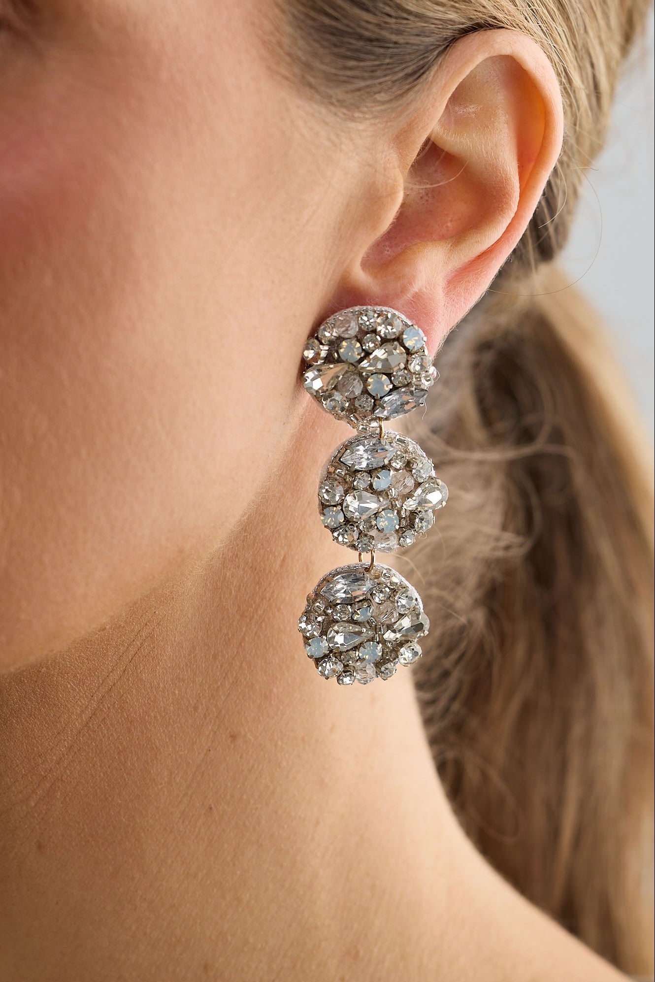 Close-up of a woman wearing a pair of silver earrings with a neutral background