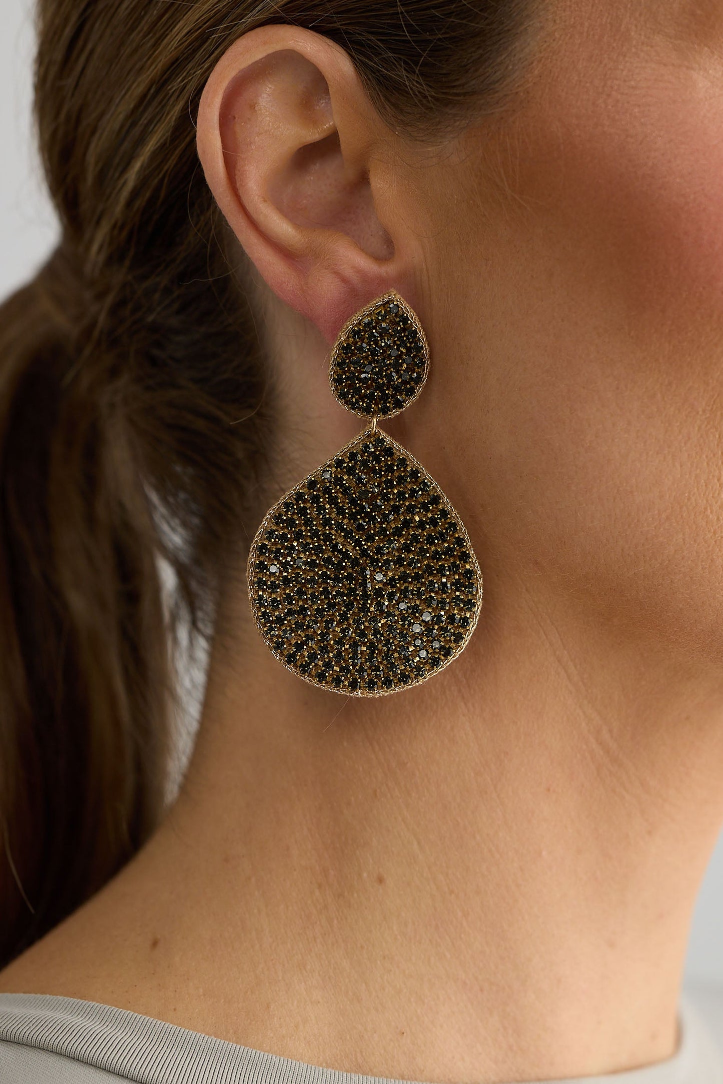 Close-up of a woman wearing a gold teardrop earring with a textured design.