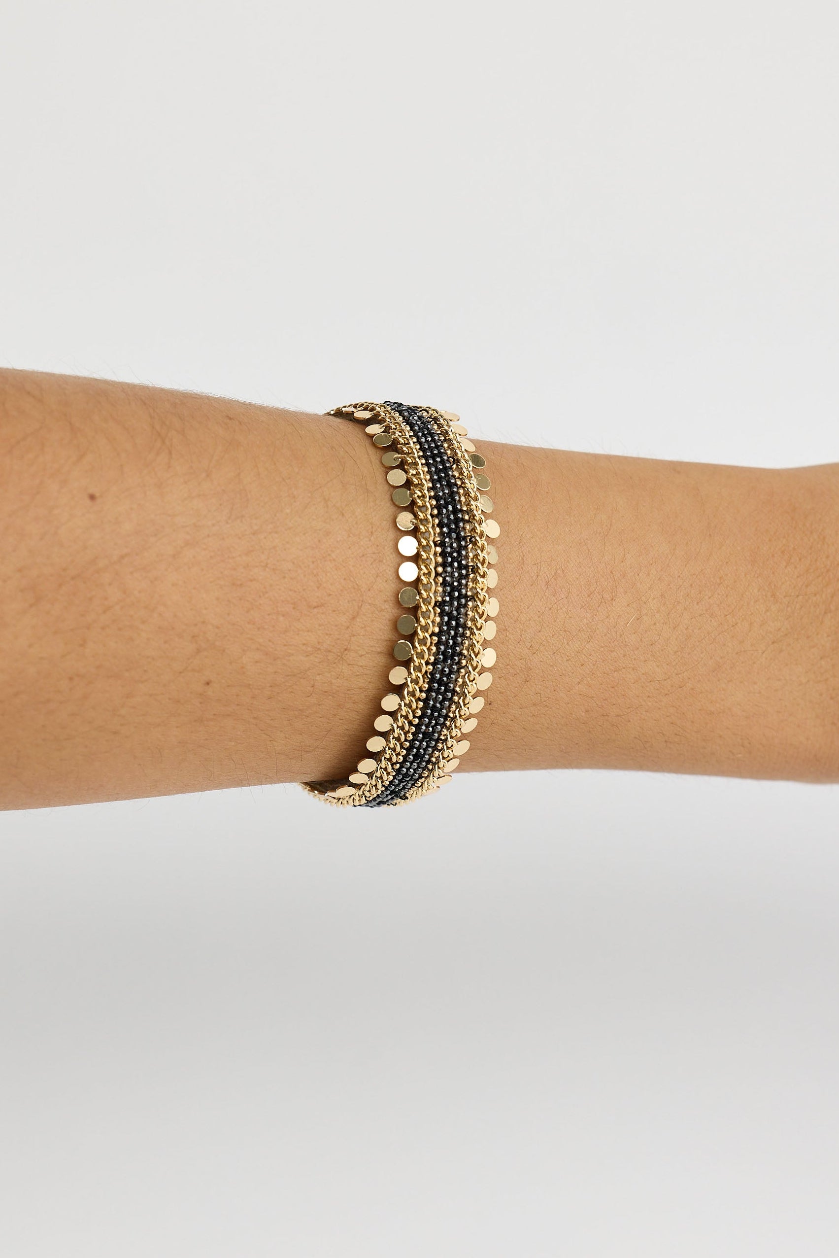 Gold and black bracelet on a wrist against a light gray background