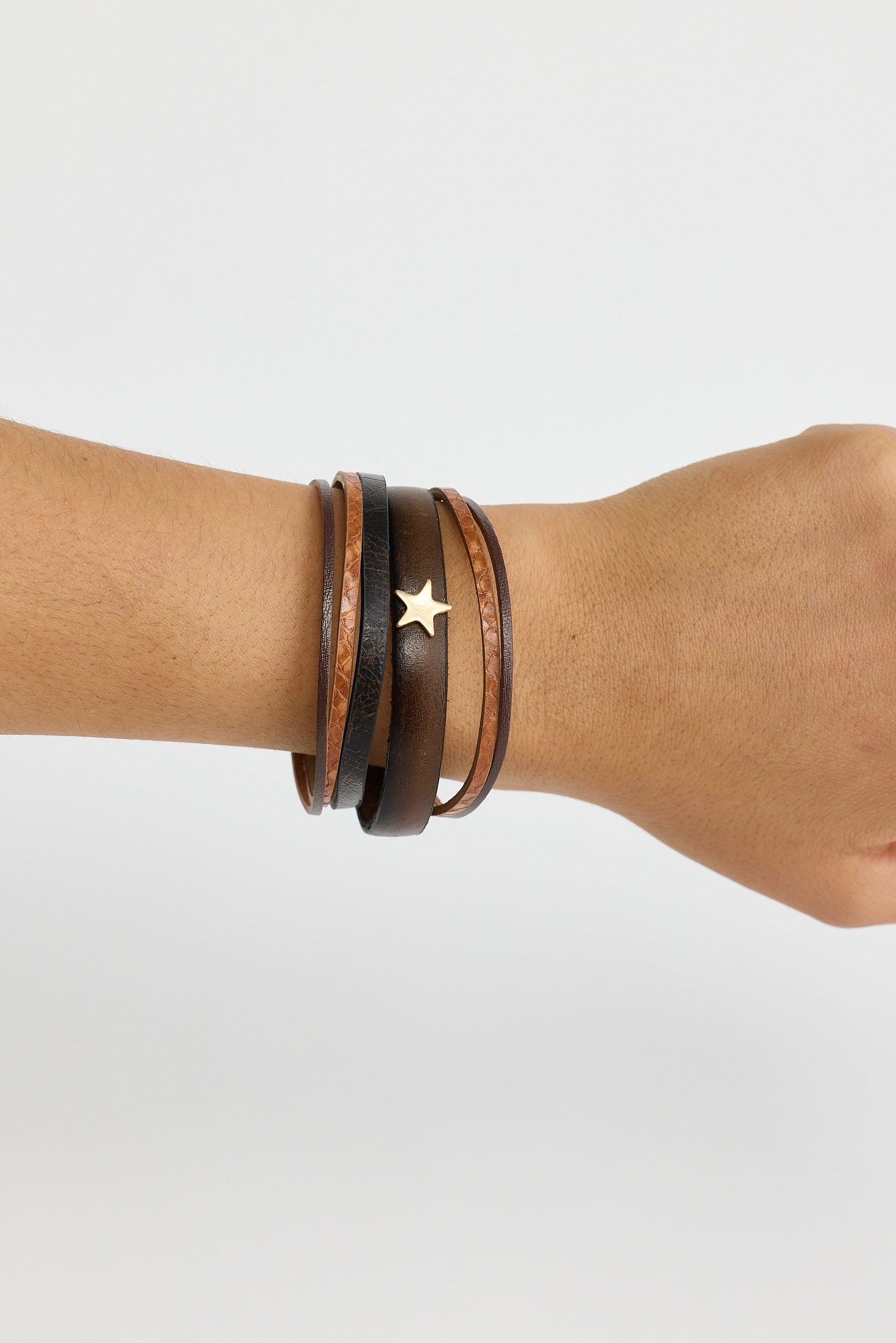 Hand wearing a brown leather bracelet with a star charm on a light gray background