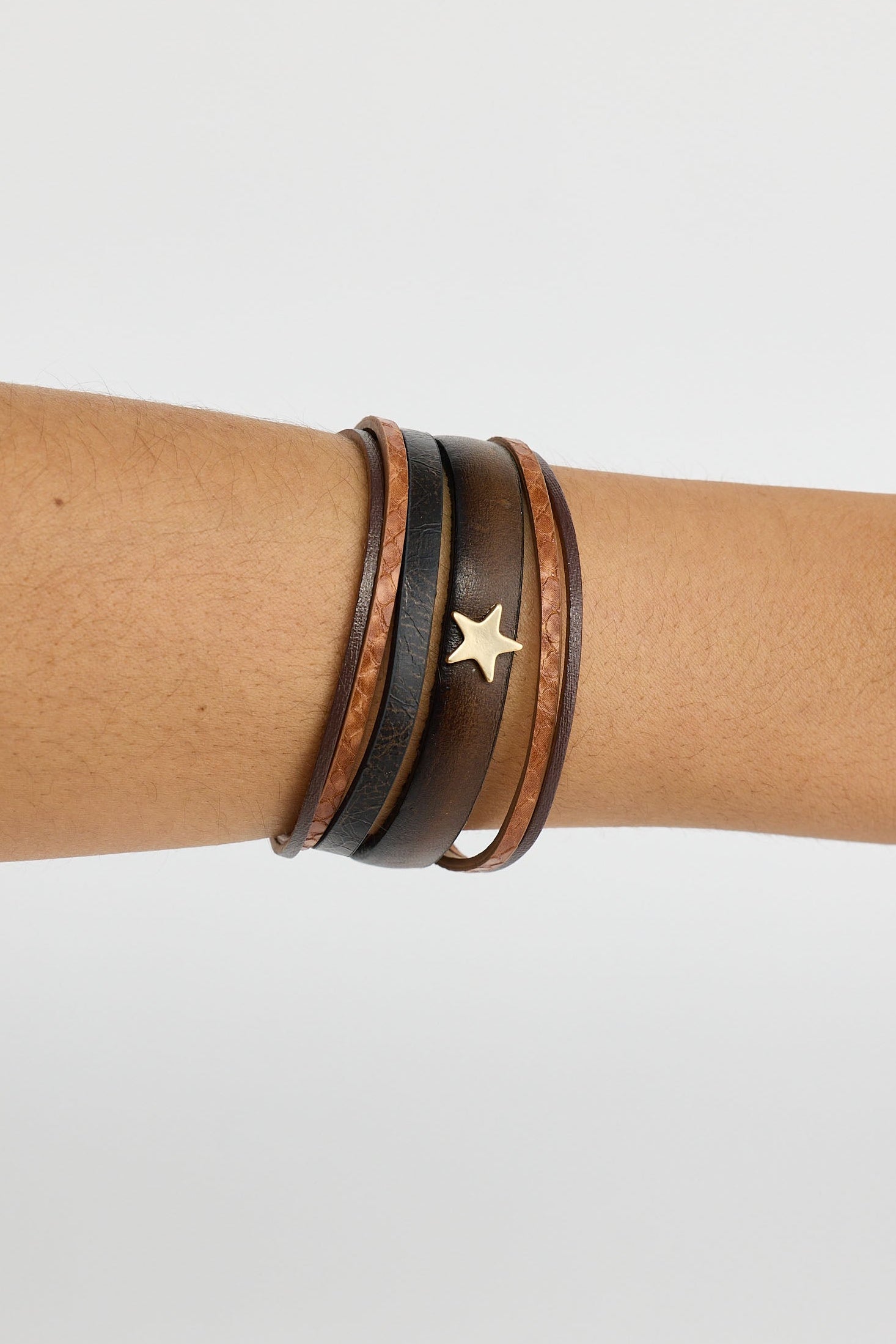 Three leather bracelets with star accents on a wrist against a light gray background