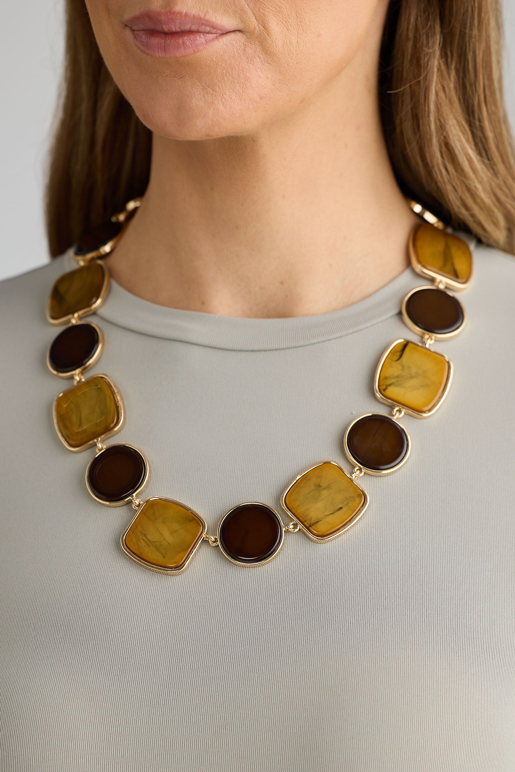 Necklace with brown and gold stones worn by a person against a neutral background