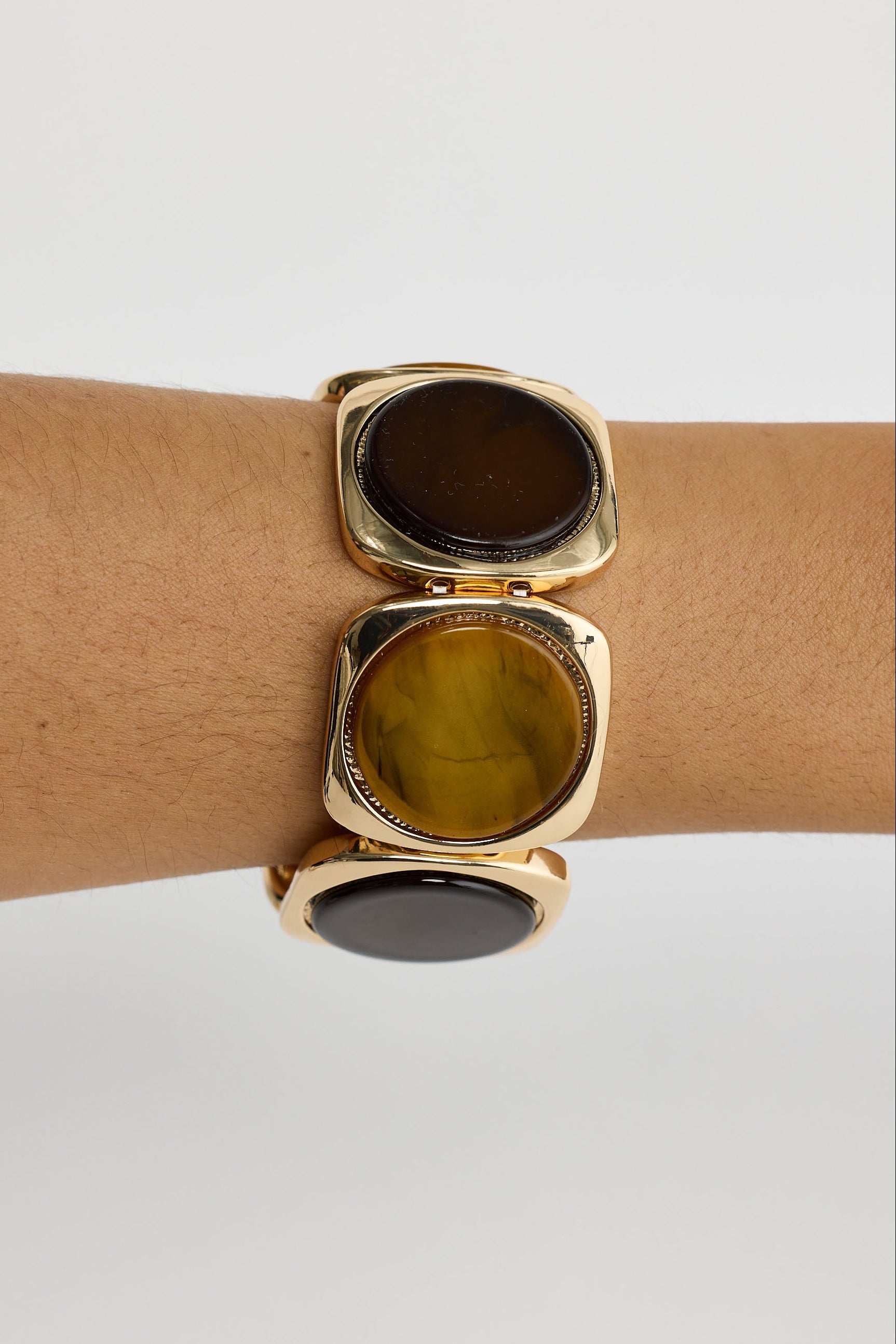Gold bracelet with large round stones on a wrist against a light gray background