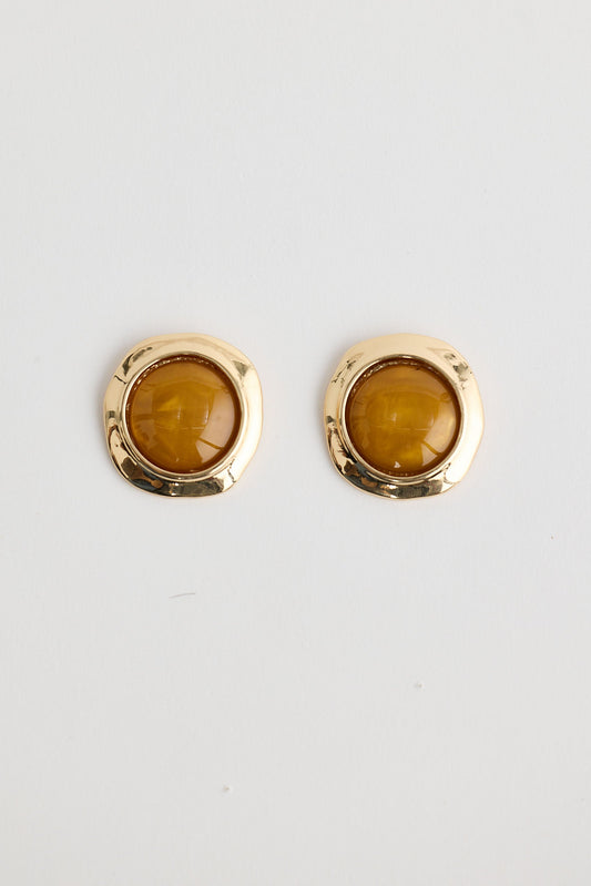 Gold earrings with amber stones on a light gray background