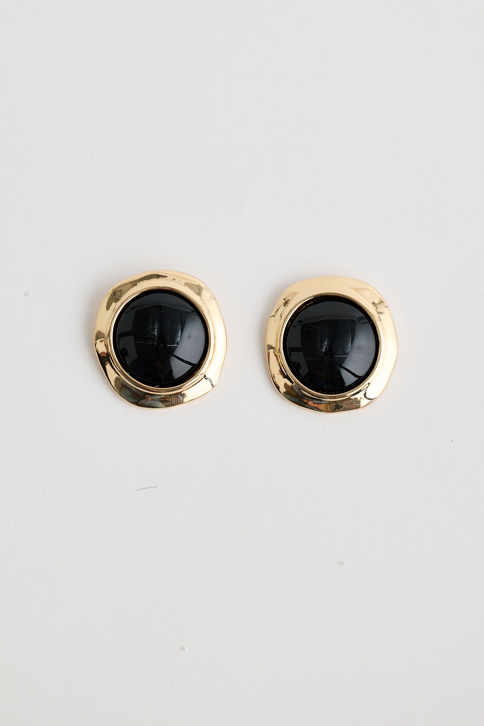 Pair of gold earrings with black stones on a light gray background
