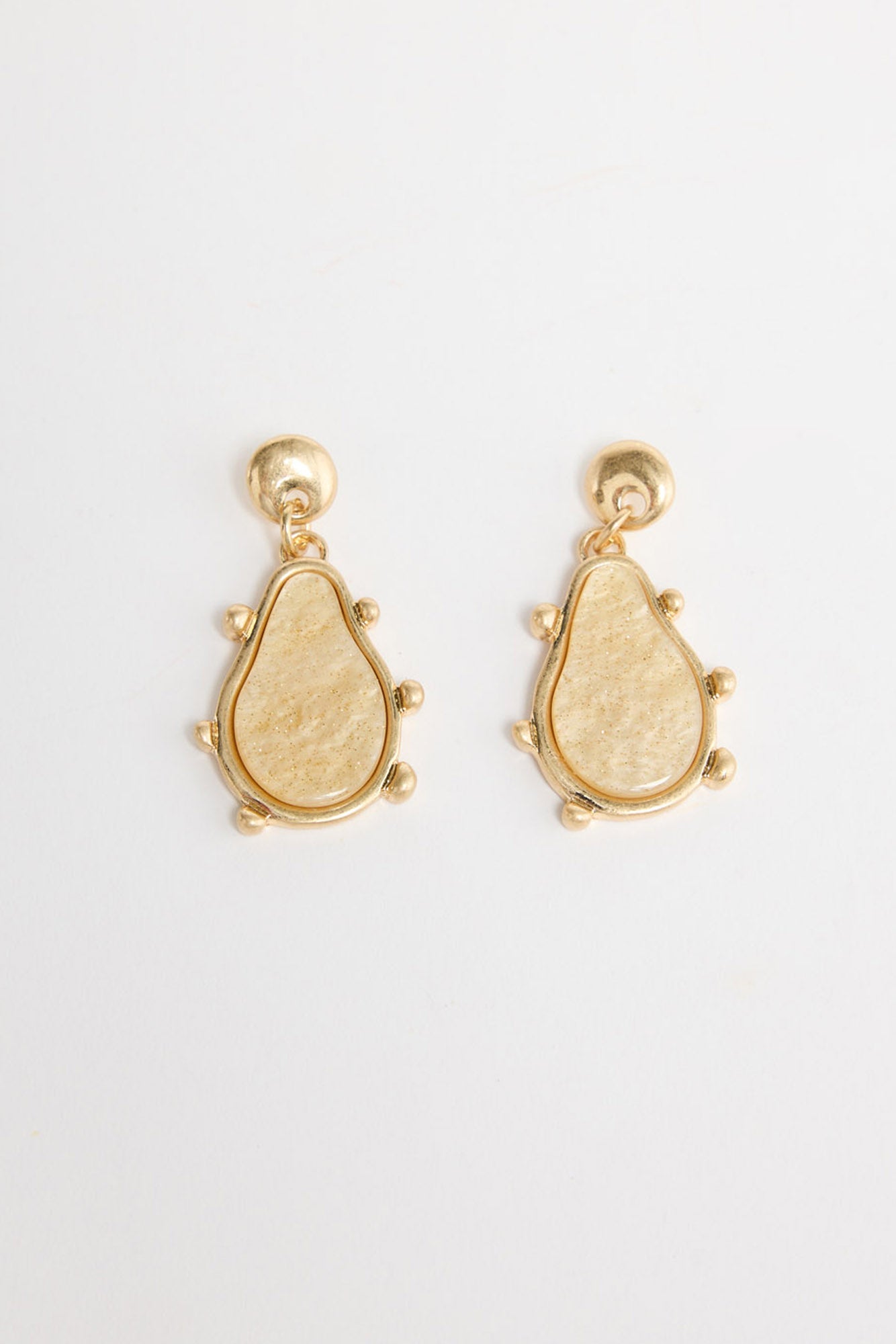 Pair of gold-tone drop earrings with a round ball stud and a teardrop-shaped cream resin pendant framed in gold with small ball accents, laid flat on a white background