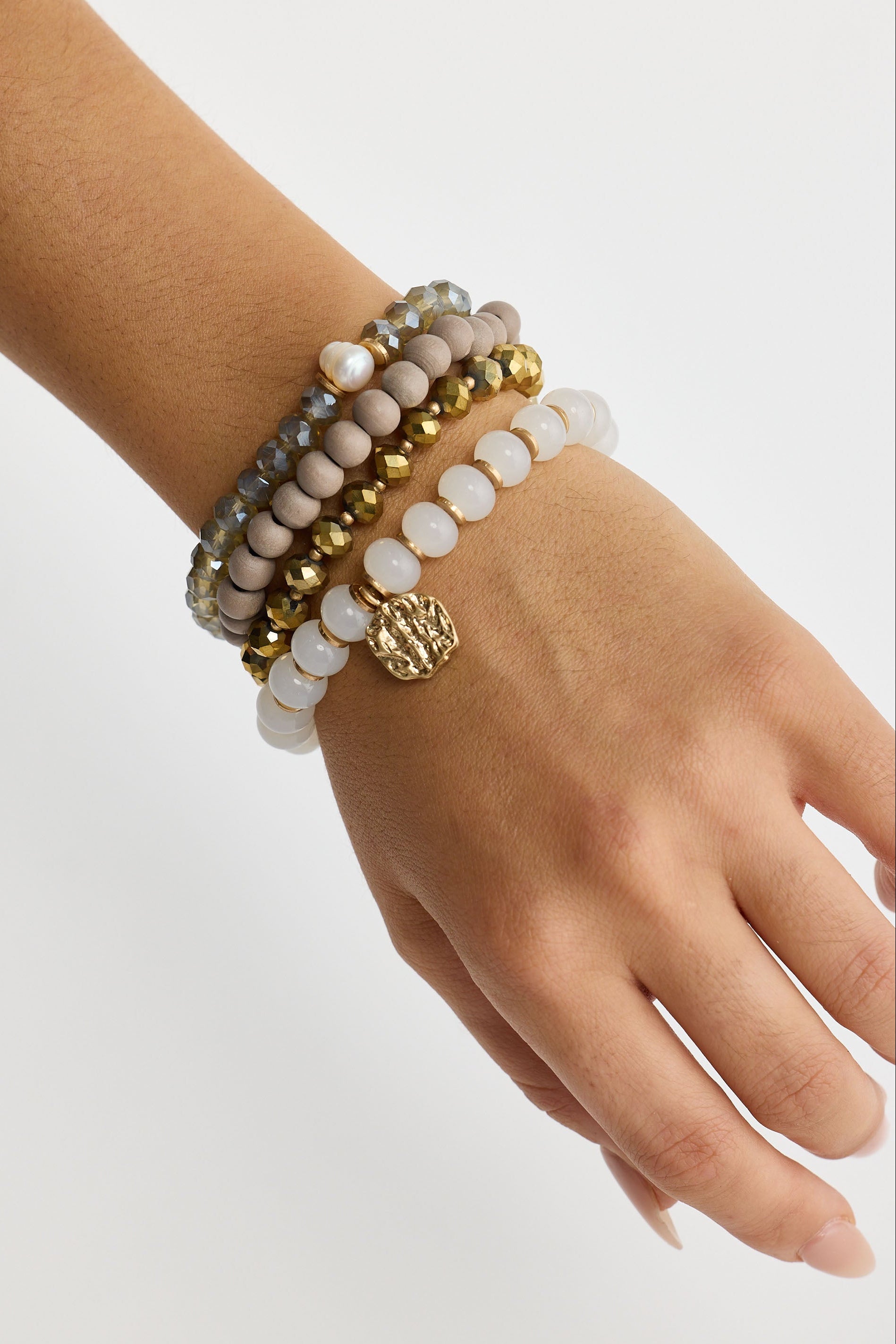 Hand wearing multiple beaded bracelets on a light background