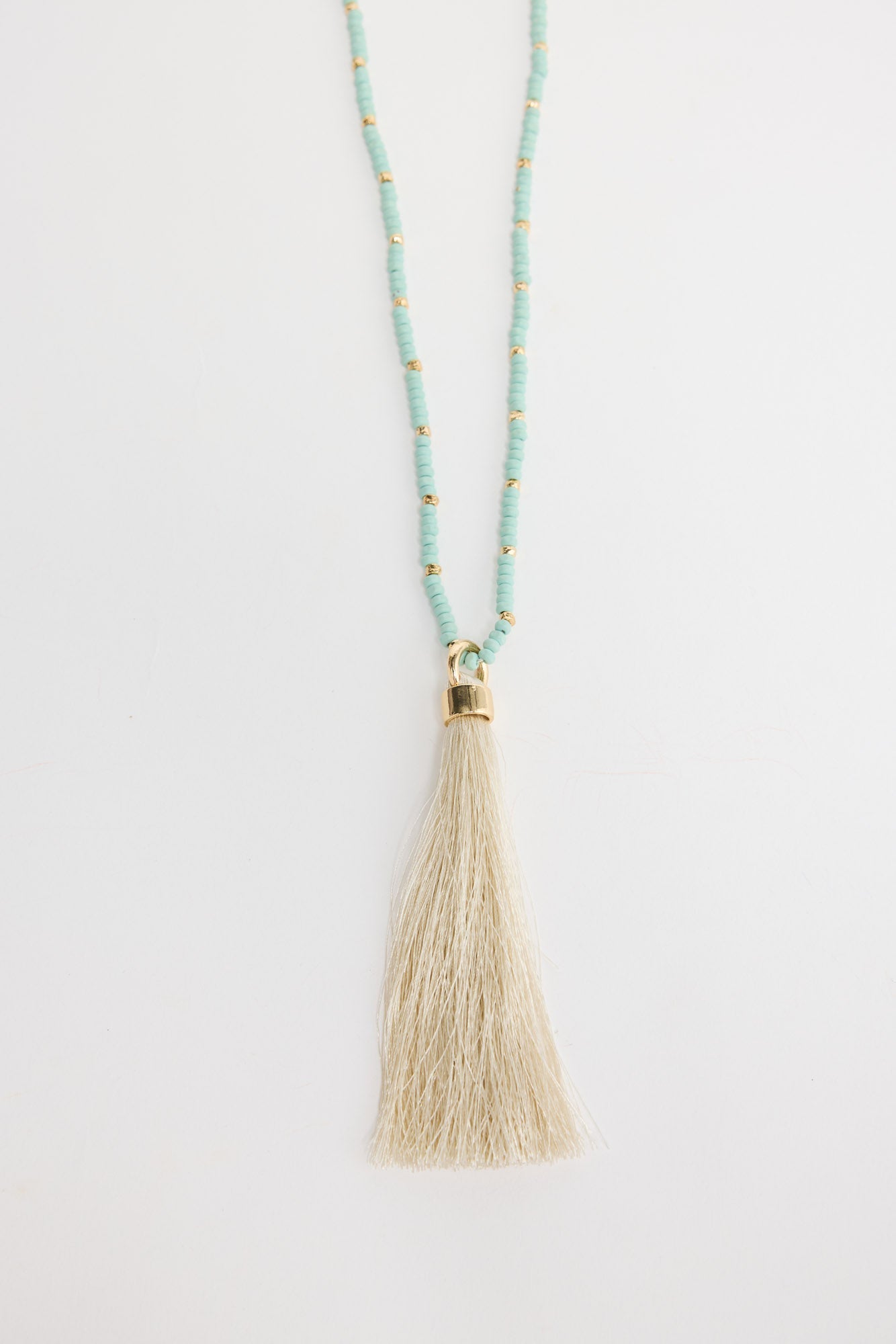 Long aqua-blue seed bead necklace with gold-tone spacer beads and a large cream silk tassel pendant with a gold cap, shown flat on a white background