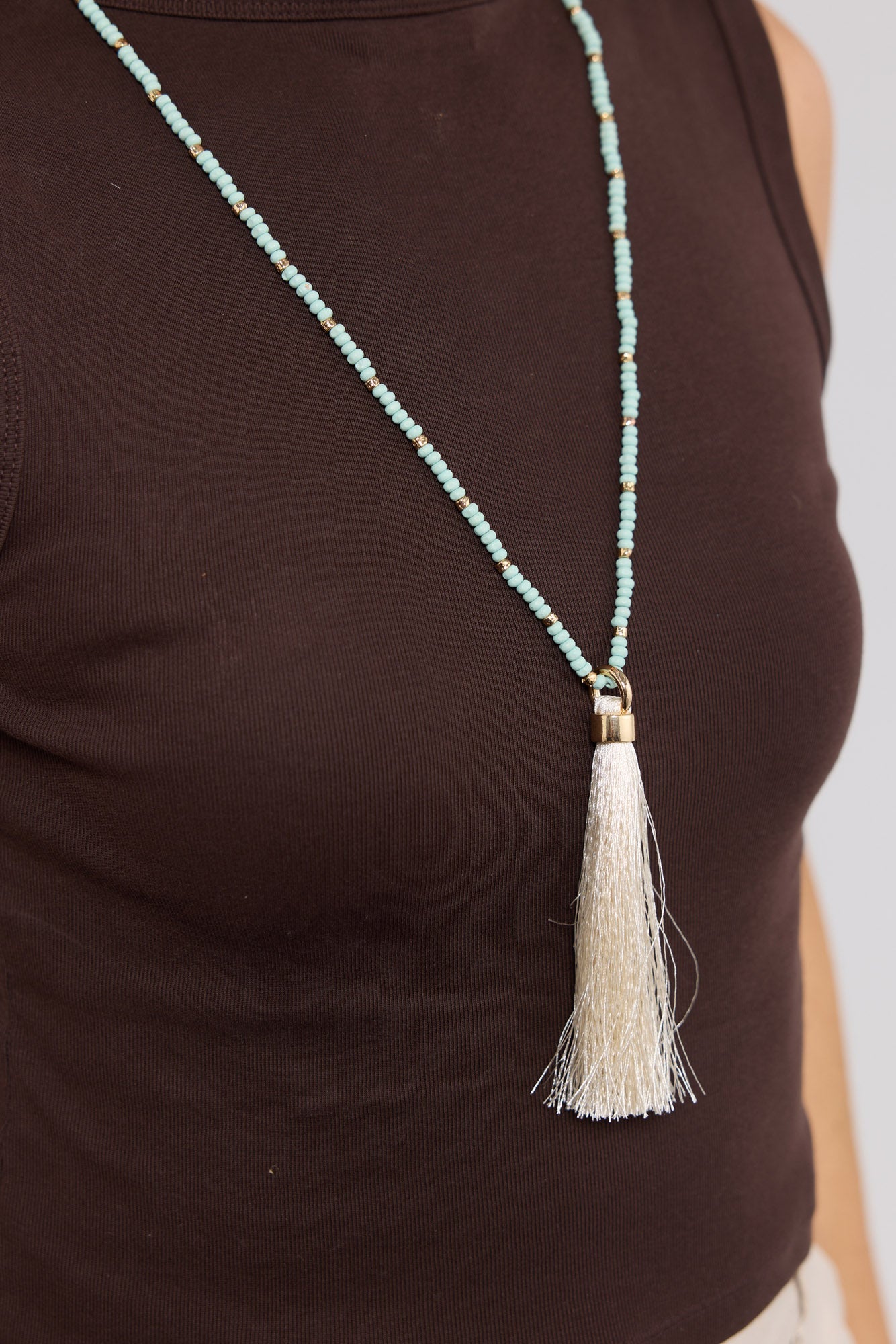 Close-up of the Mckenzie Necklace worn around the neck, showing the blue beaded strand and cream tassel pendant