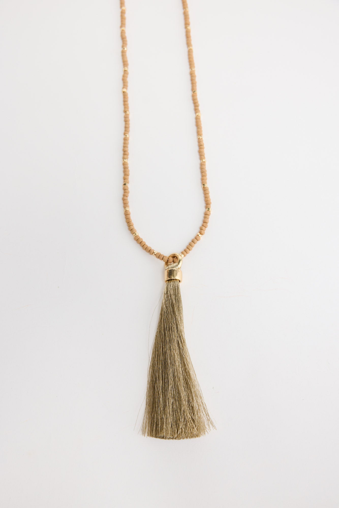 Long neutral taupe seed bead necklace with gold-tone spacer beads and a large olive-gold silk tassel pendant with a gold cap, shown flat on a white background