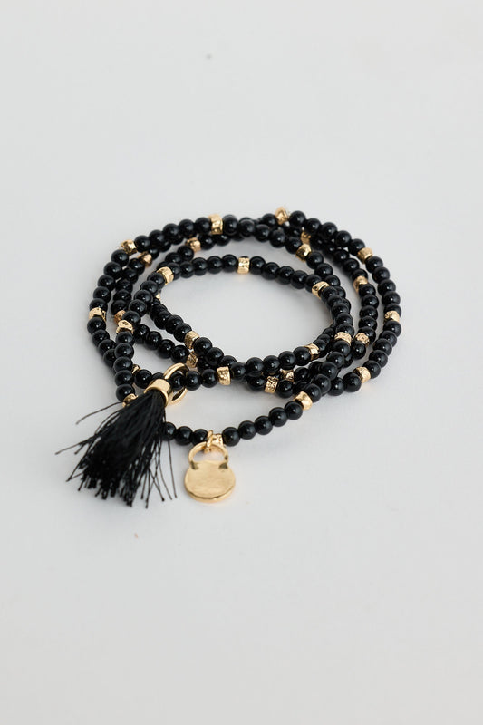 Black beaded bracelet with gold accents and tassel on a light gray background