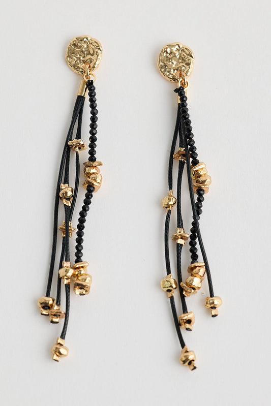 Pair of earrings with black strings and gold beads on a light gray background